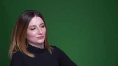Kestane rengi saçlı genç model aktif olarak müzik eşliğinde dans ediyor ve yeşil arka planda tatmin oluyor..