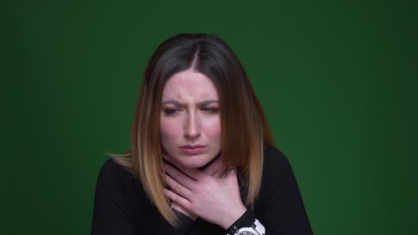 Jovem empresária com cabelo castanho tosse com uma terrível dor de garganta no fundo verde . — Vídeo de Stock