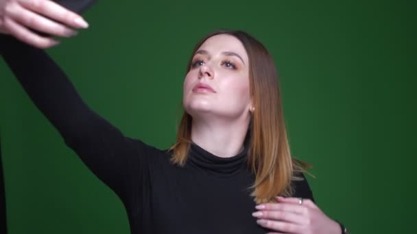 Ung affärskvinna med kastanj hår gör vackra selfie-foton på grön bakgrund. — Stockvideo