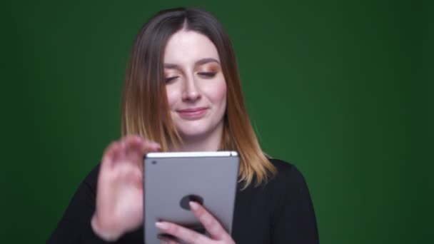 Hübsches brünettes Modell zeigt freudig den blauen Chrombildschirm des Tablets in die Kamera auf grünem Hintergrund. — Stockvideo