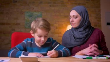Hijab Müslüman anne evde masada küçük oğlu ile ev ödevi yapıyor.