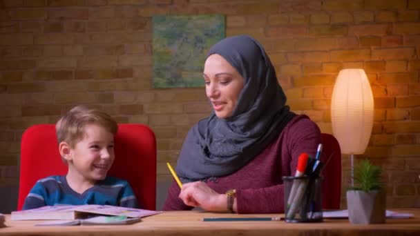 Close-up shot van moslim moeder in hijab leren brieven met haar kleine zoon aan de tafel thuis. — Stockvideo