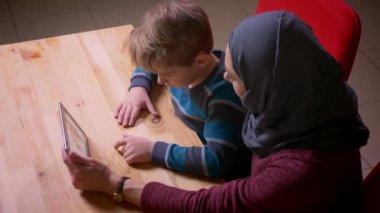 Küçük çocuk ve başörtüsü müslüman annesi tablette çizgi film izlerken profil çekimi.