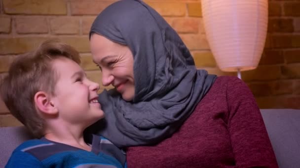 Kleiner Junge und seine muslimische Mutter im Hijab spielen mit ihren Nasen und neigen sich zu Hause hübsch aneinander. — Stockvideo