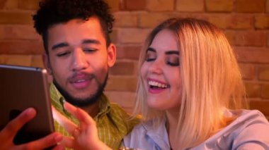 Afrikalı adam ve beyaz kız evde tablet içine mutlu izlerken kanepede oturan.