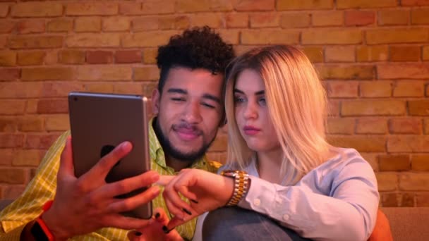 Close-up de cara africano e menina caucasiana assistindo em tablet e discutindo uns com os outros alegremente em casa . — Vídeo de Stock