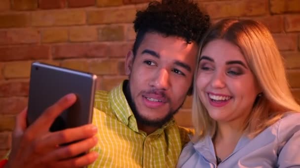 African guy and caucasian girl having a videocall on tablet being joyful and laughing happily at home. — Stock Video