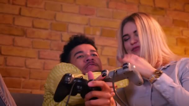 African guy and his blonde caucasian girlfriend play videogame and give five to each other at home. — Stock Video