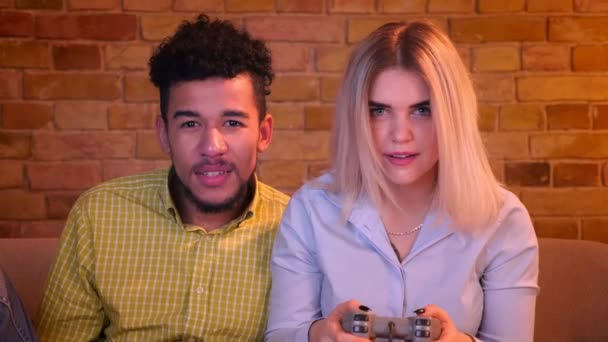 Afrikaanse kerel met zijn blonde Kaukasische vriendin spelen video game met joystick vreugdevol in gezellig huis. — Stockvideo