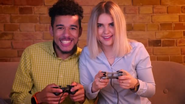 Αφρικανός τύπος με την ξανθιά Καυκάσιος φίλη του Παίξτε βιντεοπαιχνιδιών με joystick είναι παιχνιδιάρικο στο άνετο σπίτι. — Αρχείο Βίντεο