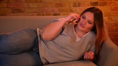 Portrait of relaxed plus size long-haired model lying on sofa talking joyfully on cellphone Chubby Stock Videos, Royalty Free Chubby Footages | Depositphotos®