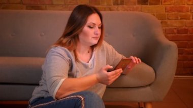 Kilolu uzun saçlı kadın serbest rahat ev atmosferinde akıllı telefon ile çalışan katta oturur.