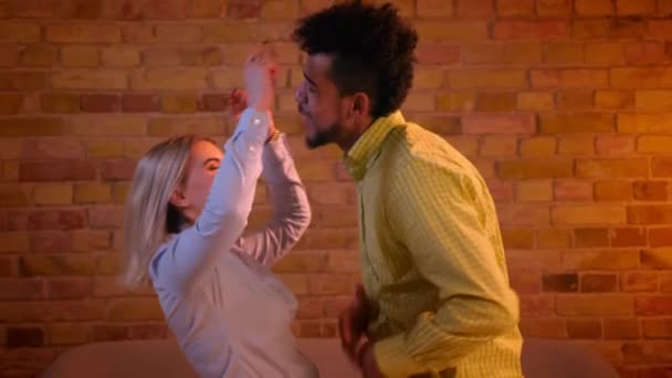 Joyful afrikansk kille och blond kaukasiska flicka dansar flirtingly med varandra i romantisk och mysig atmosfär. — Stockvideo