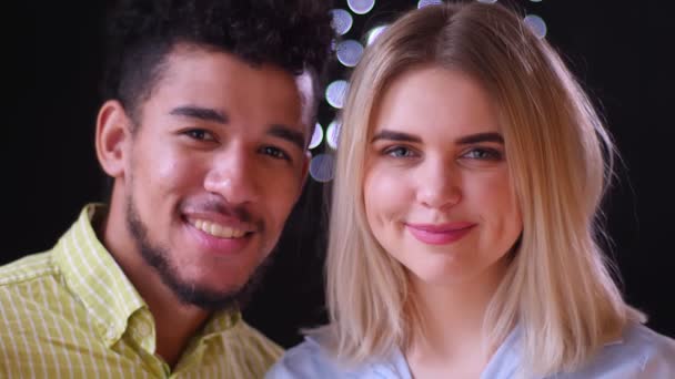 Közelkép portréja multinacionális pár néz mosolygó a kamerát homályos fények háttér. — Stock videók