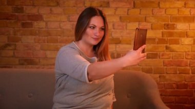 Artı uzun saç ile boyutu modeli rahat ev atmosferinde farklı taklitleri ile akıllı telefonda güzel selfie fotoğrafları yapma.