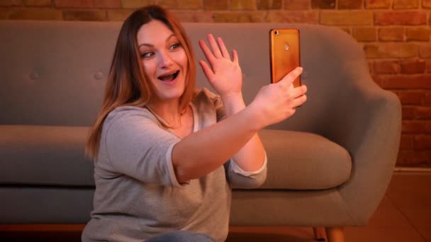 Plus size model with long hair making pretty selfie-photos giving five on smartphone in cozy home atmosphere. — Stock Video