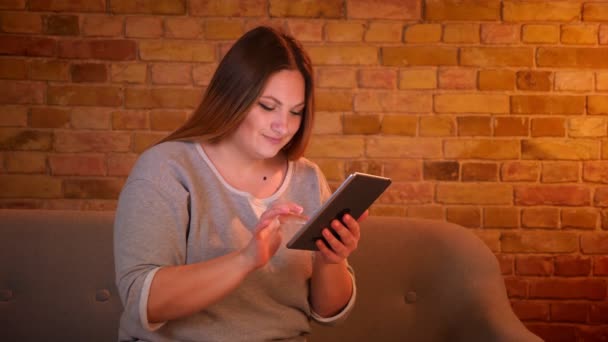 Ritratto di donna freelance sovrappeso dai capelli lunghi che lavora con attenzione con tablet in un'accogliente atmosfera domestica . — Video Stock