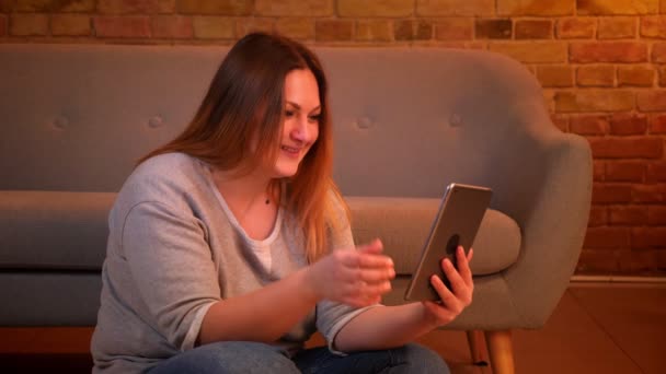 Overweight modelo feminino senta-se no chão falando em videochat no tablet ativamente e rindo em ambiente acolhedor casa . — Vídeo de Stock