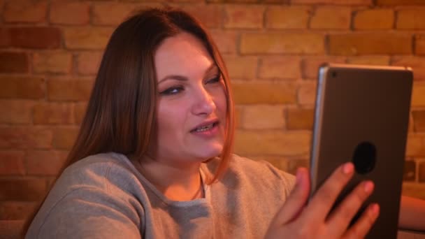 Zbliżenie portret nadwagą radosna Kobieta Model siedzi na kanapie rozmowy w videochat na tablecie w przytulnej atmosferze domowej. — Wideo stockowe