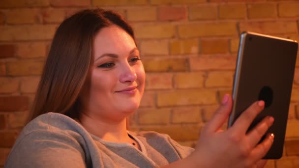 Közelről portré a túlsúlyos örömteli női modell ül a kanapén mosolyogva a tabletta otthonos otthon hangulatát. — Stock videók