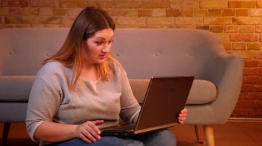 Artı boyutu modeli rahat ev atmosferinde düşünceli olmak dizüstü bilgisayar da videochat konuşurken katta oturur.