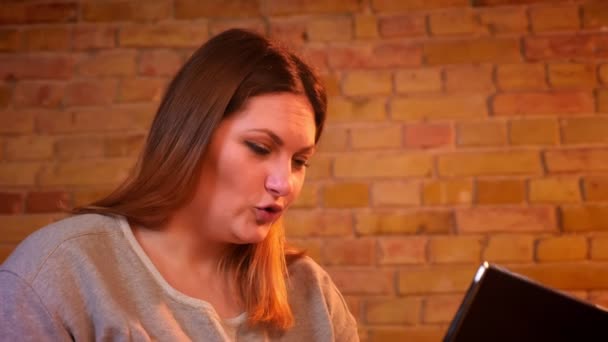 Portrait of overweight joyful female student sits on sofa having a videocall on laptop in cozy home atmosphere. — Stock Video