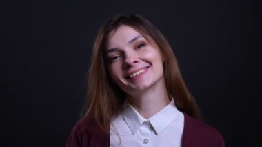 Siyah arka planda kameraya utangaç ve güzel bir gülümseme ile izlerken genç esmer iş kadını Portresi.