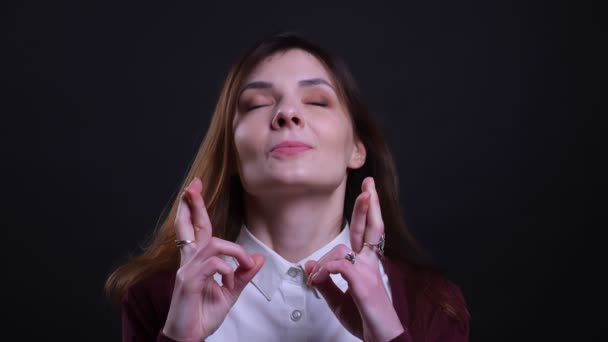 Retrato de joven empresaria morena con los ojos cerrados reza con los dedos cruzados sobre fondo negro . — Vídeos de Stock