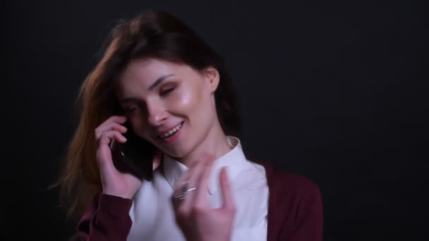 Porträtt av ung brunett affärskvinna pratar på mobiltelefon och skrattar glatt på svart bakgrund. — Stockvideo