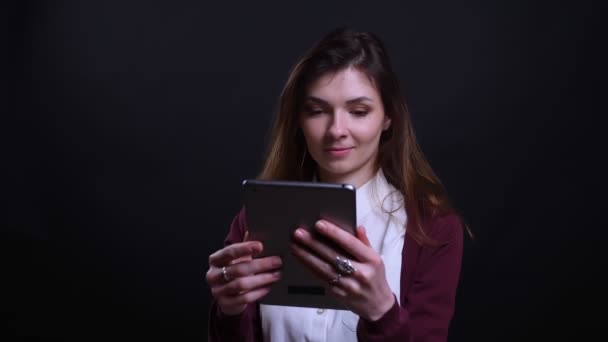 Retrato de joven mujer de negocios morena mirando en la tableta con gran interés en el fondo negro . — Vídeo de stock