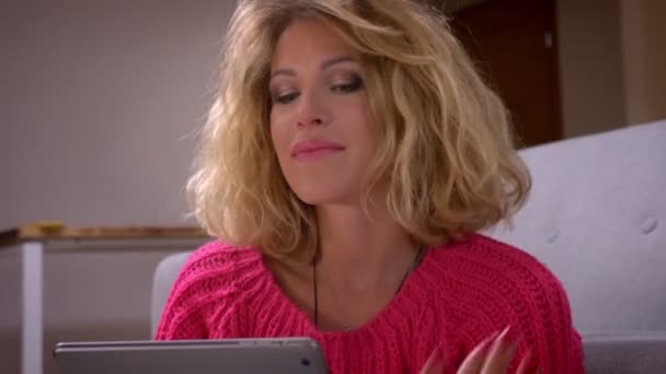 クローズアップショット主婦は、タブレット上のビデオチャットで話し、居心地の良い家庭の雰囲気の中できれいにキスを吹いて髪を調整. — ストック動画