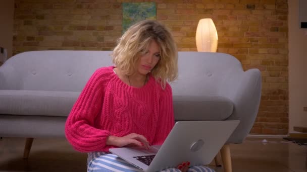 Primo piano di casalinga in maglione rosa che naviga attentamente nel computer portatile con grande concentrazione in atmosfera domestica . — Video Stock