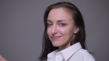 Beyaz gömlekli yetişkin çekici beyaz kadın closeup portre gülümseyerek ve gri izole arka plan ile kamera bakarak saçlarını sabitleme