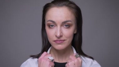 Beyaz gömlekli yetişkin çekici beyaz kadın closeup portre gülümseyerek ve gri izole arka plan ile kamera önünde poz saçlarını sabitleme