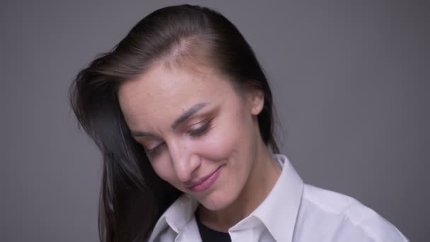 Gros plan portrait d'adulte attrayant caucasien femelle dans une chemise blanche regardant la caméra souriant avec timidité avec fond isolé sur gris — Video