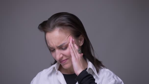 Closeup retrato de adulto atraente caucasiano fêmea ter uma dor de cabeça e estar cansado na frente da câmera com fundo isolado em cinza — Vídeo de Stock