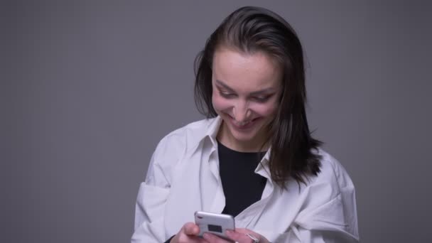 Close-up portret van volwassen aantrekkelijke blanke vrouw met behulp van de telefoon glimlachen en lachen met achtergrond geïsoleerd op grijs — Stockvideo