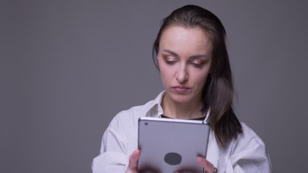 Close-up portret van volwassen aantrekkelijke blanke vrouw met behulp van de Tablet en glimlachend met achtergrond geïsoleerd op grijs — Stockvideo