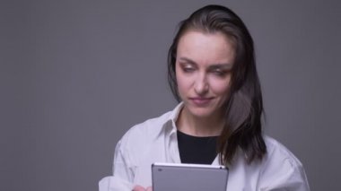 Tableti kullanan ve gri üzerine izole edilmiş arka planlı kameraya gülümseyen yetişkin çekici beyaz kadın closeup portre