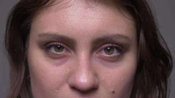 Съемки крупным планом взрослого привлекательного женского лица брюнетки с закрытыми глазами, открывающимися и смотрящими на камеру с изолированным на сером фоне — стоковое видео