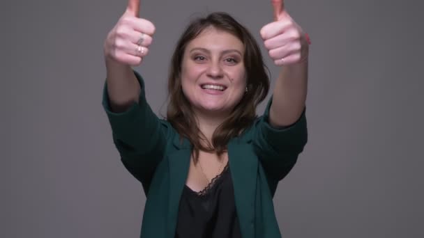 Close-up shoot van volwassen aantrekkelijke brunette vrouw die duimen omhoog kijkt naar de camera met achtergrond geïsoleerd op grijs — Stockvideo