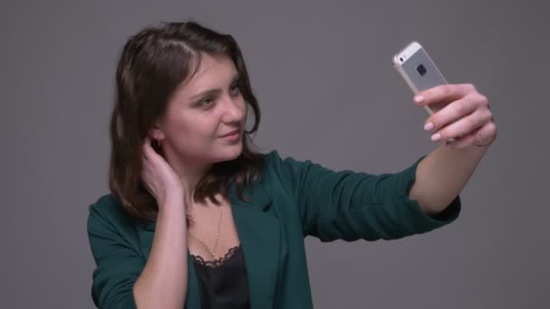 Close-up tiro de adulto atraente morena fêmea tomando selfies no telefone com fundo isolado no cinza — Vídeo de Stock