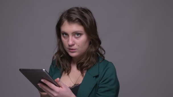 Closeup lő felnőtt vonzó barna női textil a tablettát, és nézte a kamerát háttérrel izolált szürke — Stock videók