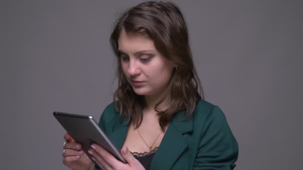 Close-up tiro de adulto atraente morena feminina usando o tablet e mostrando tela de croma verde para câmera com fundo isolado em cinza — Vídeo de Stock