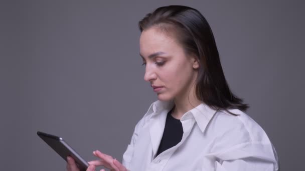Nahaufnahme Porträt von erwachsenen attraktiven kaukasischen Frau mit dem Tablet und zeigt grünen Bildschirm vor der Kamera mit Hintergrund isoliert auf grau — Stockvideo
