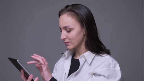 Close-up portret van volwassen aantrekkelijke blanke vrouw met behulp van de Tablet en het tonen van groene Chroma scherm naar camera met achtergrond geïsoleerd op grijs — Stockvideo