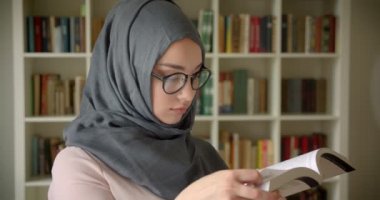 Başörtüsü ve gözlük kütüphanede özenle kitap okuma Müslüman öğrencinin profil portresi.
