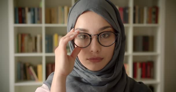 Portré muzulmán üzletasszony a hidzsáb és szemüveg figyelte nyugodtan a kamera a könyvtárban. — Stock videók
