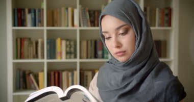 Başörtüsü okuma kitabı müslüman öğrencinin profil portresi kütüphanede kameraya özenle gülümsüyor.