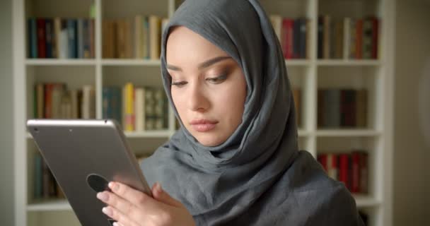 Tabletle çalışan türbanlı Müslüman öğrencinin profil portresi kütüphanede kameraya sakince bakıyor. — Stok video